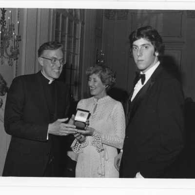 Donald I. MacLean, S.J., presenting alumni award to Terrence Diamond with Mrs. William (Pat) Diamond, watching, at alumni awards dinner, c. 1980.
