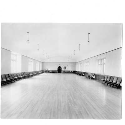 Interior view of college auditorium in Barbelin Hall. The room is empty and chairs are lined up along the walls.