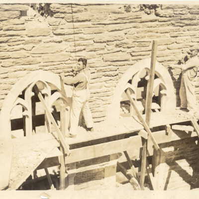 Exterior view of Barbelin building under construction with two stone masons on scaffolding working on gothic tracery.