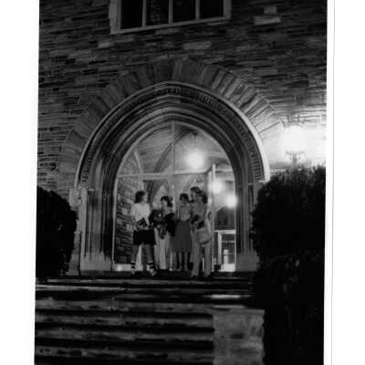 Female students at central arch main entrance to Barbelin building in evening.