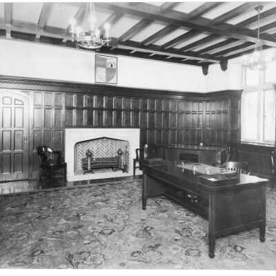 Interior view of Dean's office in Barbelin building with fireplace, desk, oak wainscoting, and oriental rug.