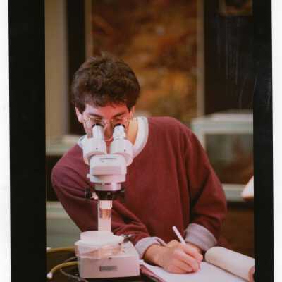 Male student looking through microscope during experiment in science laboratory.
