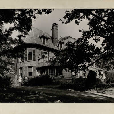 Exterior view of Quirk Hall with several students standing on lawn and on porches.