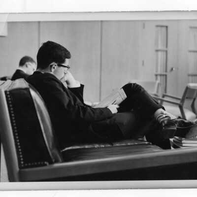 Two students in coat and tie studying in lounge chairs.