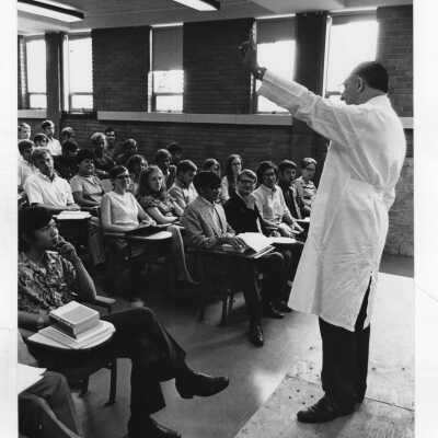 Louis S. Marks (Biology) standing in front bookcase wearing lab coat; and Louis S. Marks teaching a class.