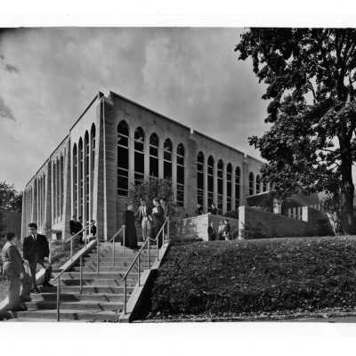 Exterior view of Drexel Library with students talking to Father Baum (?) and others.