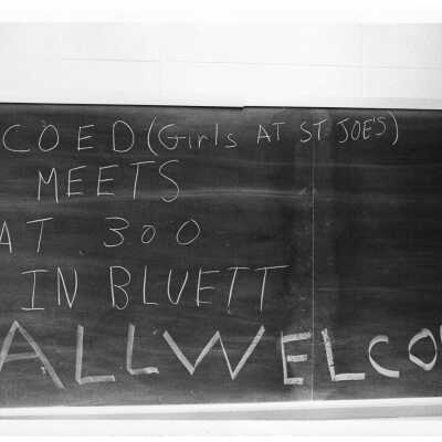 Sign on blackboard announcing co-ed girls meeting in Bluett Theater.