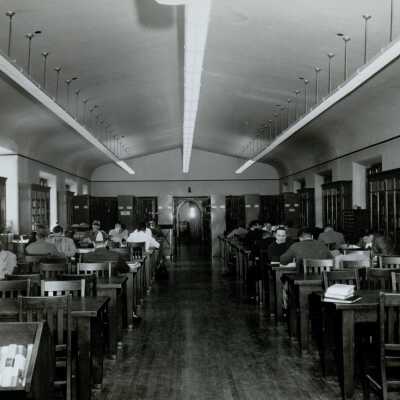 Interior view of library with students studying at desks in Barbelin building with several students wearing SJC striped caps.