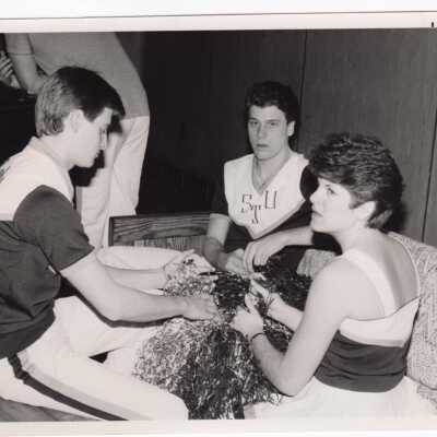 Men and women cheerleaders making pom poms.