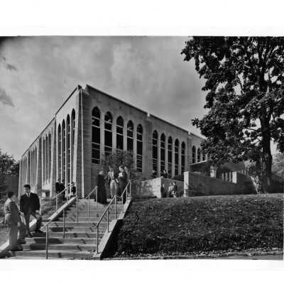Exterior view of Drexel Library with students talking to Father Baum (?) and others.