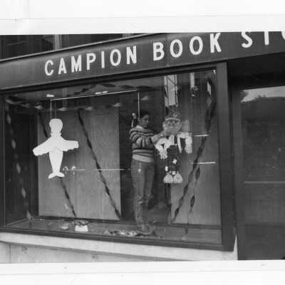 Student standing in Campion bookstore window putting up Halloween decorations.