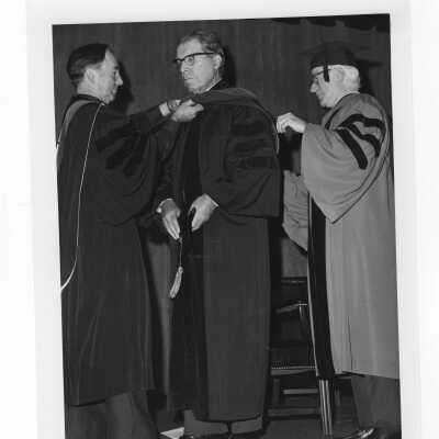 Terrence Toland, S.J., conferring honorary degree to Harry R. Halloran (?) with Dr. Lawrence J. Bell (?) assisting during convocation, December 17, 1975.