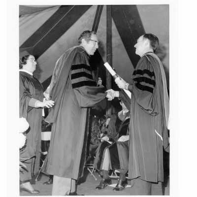 Terrence Toland, S.J., conferring honorary degree on F. Otto Haas (honorary consul general, Federal Republic of Germany) during 1976 graduation/commencement with Herta M. Stephenson watching.