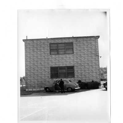 View of couple standing near car outside of veterans barracks located near the Cardboard College (also known as Barbelin Annex).