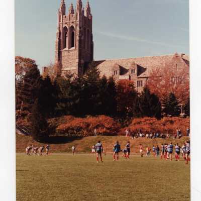 Men's rugby game in the fall on Finnesey Field with Barbelin Hall in background.