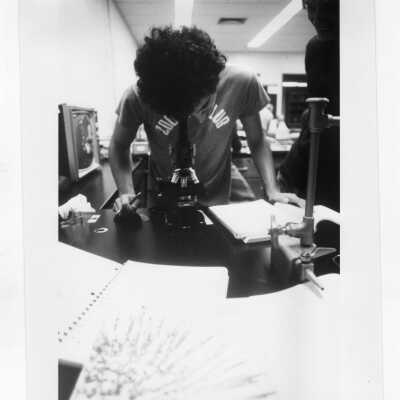 Male student looking through microscope in science laboratory.