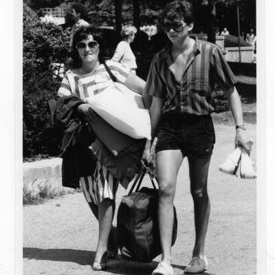 Male student and his mother packing and leaving at end of year? She is dressed in striped dress and he is dressed in striped shirt and shorts.