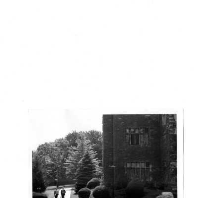 Exterior side view of Barbelin building with ivy on wall and two men walking.
