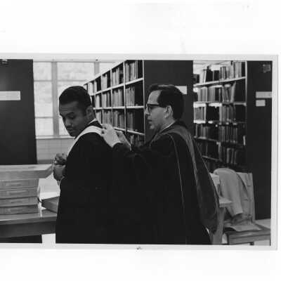 Inauguration of President Terrence Toland, S.J., November 14, 1968. Before ceremony, two faculty members, Gerard A. Ferere and Lawrence Baccile, assist each other with robing in academic garb in Drexel Library.