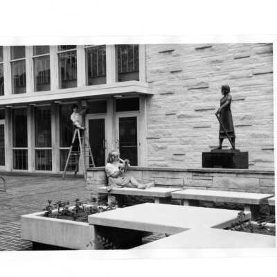 Exterior view of Villiger (later Post) with statue of Saint Joseph the Worker, and student sitting on bench reading and workman on ladder.