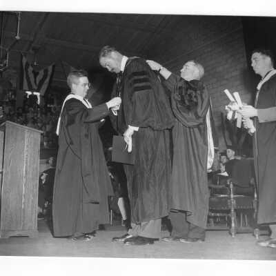 John J. Long, S.J. helping Thomas F. Murphy with academic robes during 1950 graduation/commencement ceremony. Father Drane and Michael Boland also present.