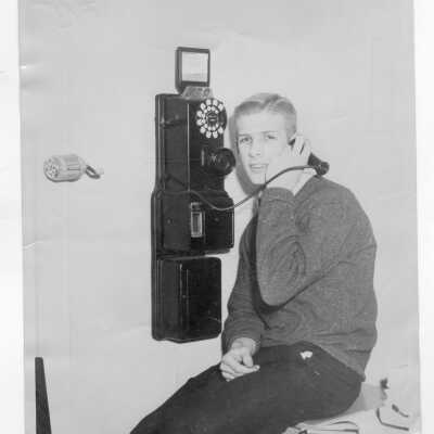 Student resident of Barry Hall talking on pay telephone next to pencil sharpener on wall.