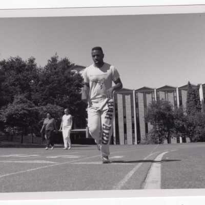 Student running on track with two neighborhood (?) women walking and Bellarmine Hall in background.