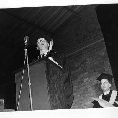 John J. Hearne addressing graduating students at 1953 graduation/commencement ceremony with Frank McG. Nugent, S.J. looking on.