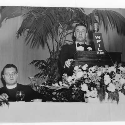 Edward G. Jacklin, S.J., listening to speaker (John Nason or Joseph P. Tully?) during banquet held in Field House as part of centennial anniversary celebration.
