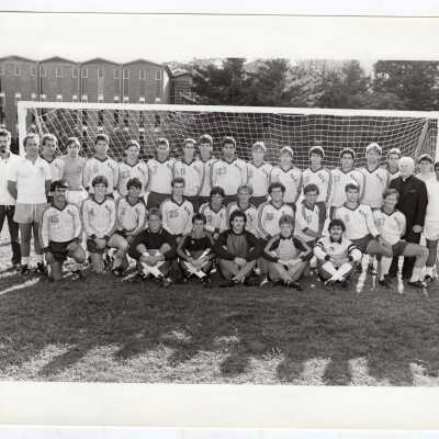 Group photo of men's soccer team with Emory Ross, S.J. and Bellarmine building in background.