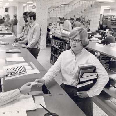 Internal view of Drexel Library with stairwell, students checking out books at circulation desk and others studying at desks.