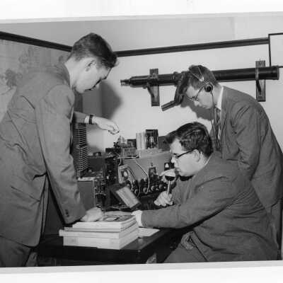 Three members of student Radio Club working with equipment and speaking into microphone. (Connected to Physics Department?)
