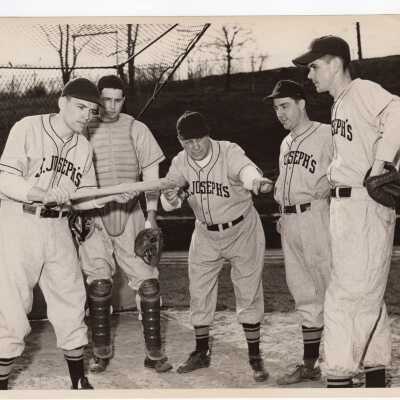 Some members of 1952 Saint Joseph's College baseball team, including Jack McKeon, Al Readinger, Coach Pep Young, Don Barr, and Joe Brennan standing near pitcher's mound.