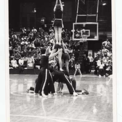 Men and women cheerleaders in pyramid during basketball game.