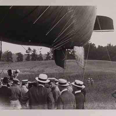 Group surrounding tethered dirigible in a field