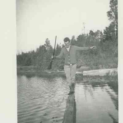 Man with rifle on a log in the water