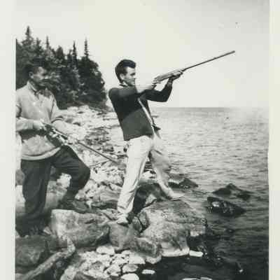 Two men with rifles on the shore of Lake Huron