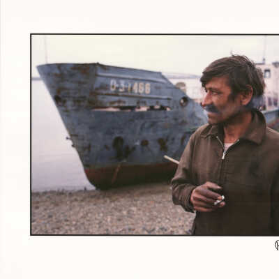 A Siberian fisherman smokes next to his fishing vessel on the shore of the Tom River, Tomsk, Russia