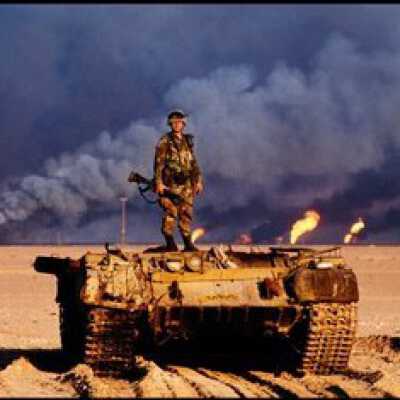 An American soldier stands on top of a destroyed Iraqi tank. Kuwaiti oil wells, ignited by Saddam's retreating forces, burn in the distance, Kuwait