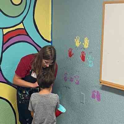 Artist working with young contributer.: A woman and child engage in a colorful art project, painting handprints near a vibrant mural.