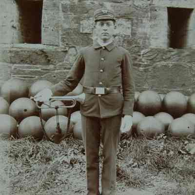 Single man in uniform with bugle against a pile of cannon balls