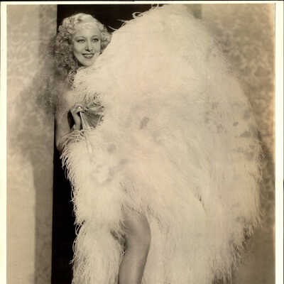 Photo - Sally Rand-Standing by wall covered with feather fan-leg showing-B&W
