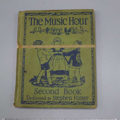Hardback book with green and blue cover, images of dancing children surrounded by a frame of music notes