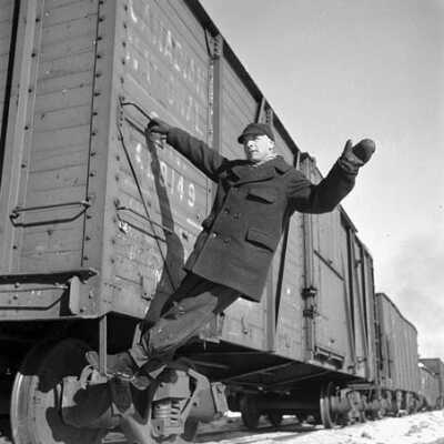 Photograph, Brakeman holds on to a box car on the Canadian National railways line.