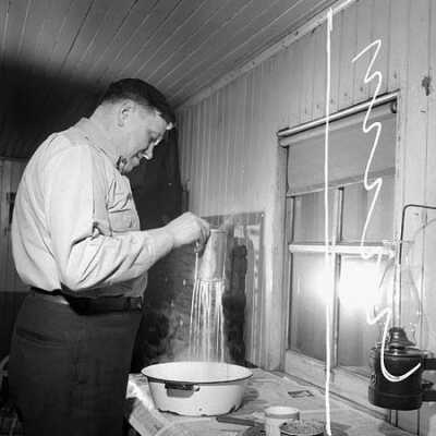 Photograph, Conductor C.E. Rose dips a perforated can containing soap scraps into dishwater to wash dishes in his railway caboose.