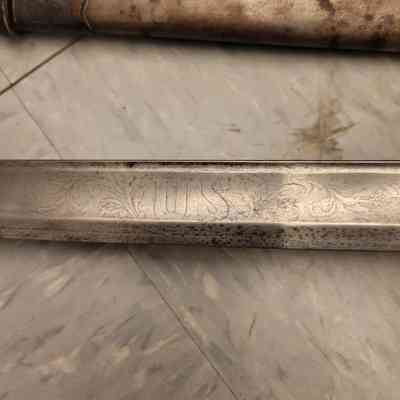 The image shows an intricately engraved sword blade with "U.S." inscribed and a worn metal