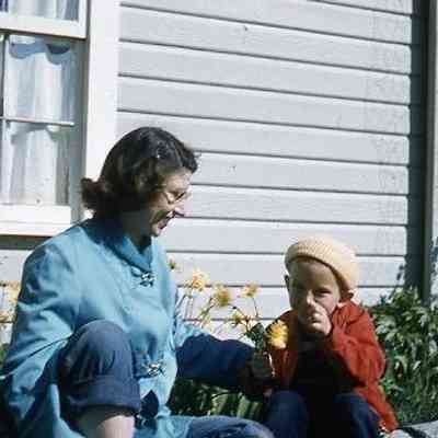 66. JJC smiling and KJH sitting in backyard with flowers: Zylstra House - April 1957