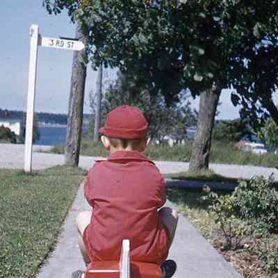 75. KJH riding pedal car on sidewalk, Penn Cove in background: Coupeville - June 1957
