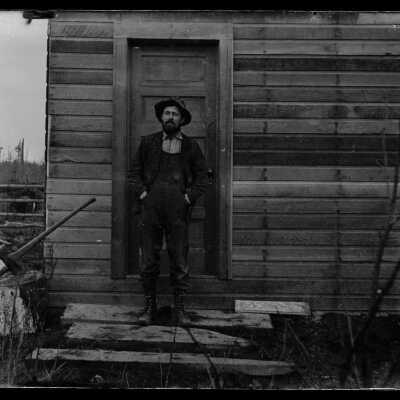 Man on cabin steps: Origsize: 4x5; Origformat: Negative