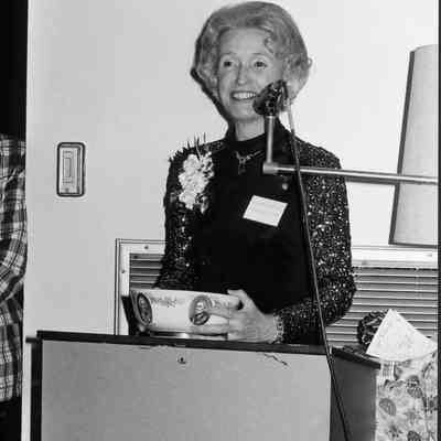 Woman holding bowl speaks at microphone.